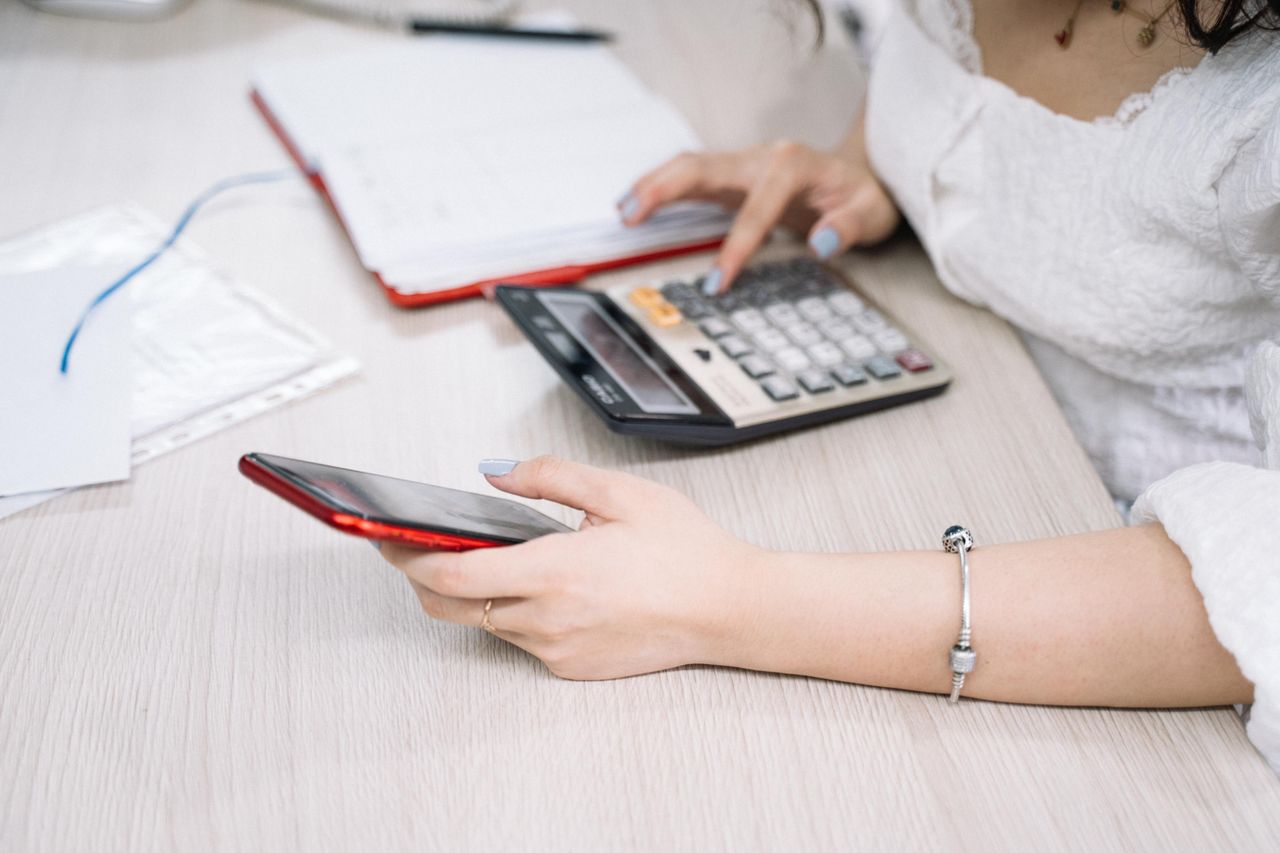 about-us-02 A woman managing finances using a calculator and smartphone at her desk, showcasing multitasking in an office setting.