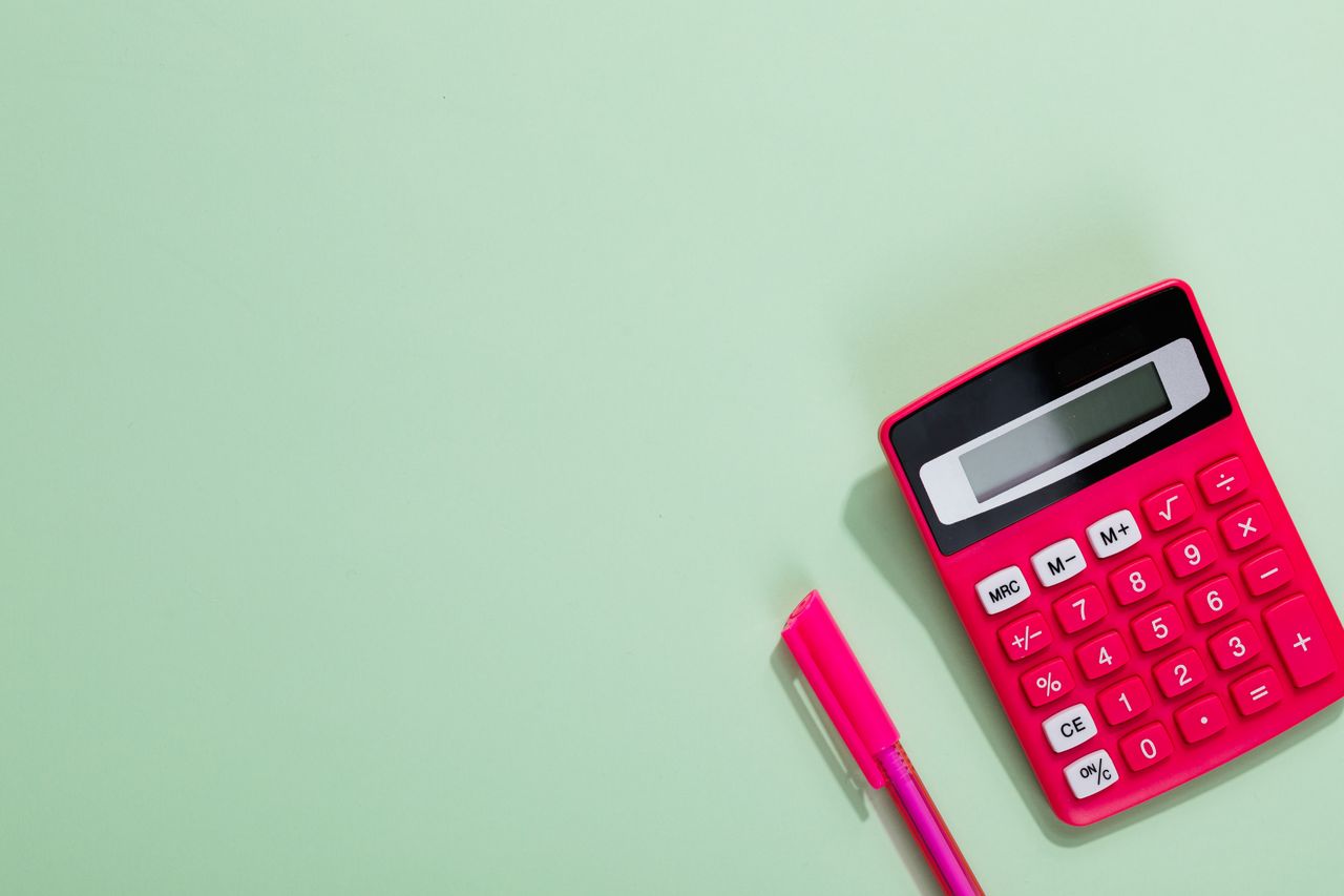 services-03 Pink calculator and pen on a pastel green background with copy space.