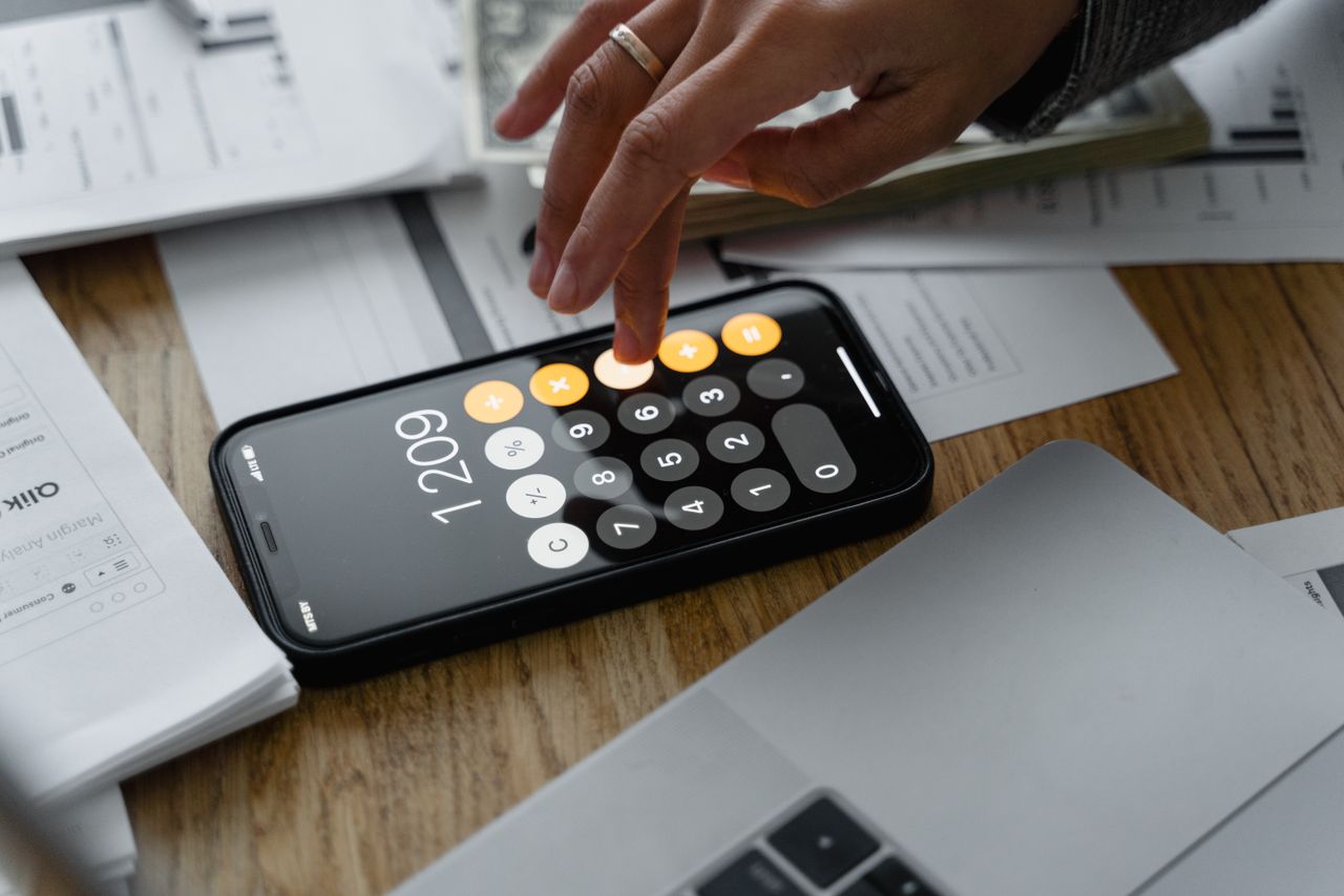 about-us-01 Close-up of a person using a smartphone calculator on a table with documents for financial calculations.
