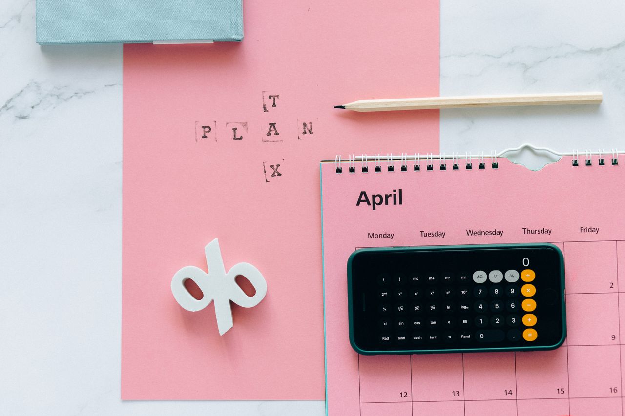 heros-img Flat lay of April calendar with calculator, pencil, and pink background for financial planning.