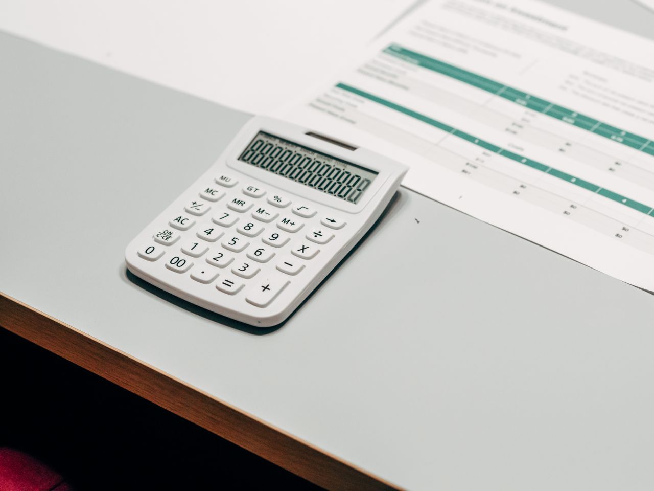 services-02 Close-up of a white calculator next to a financial spreadsheet on a desk.